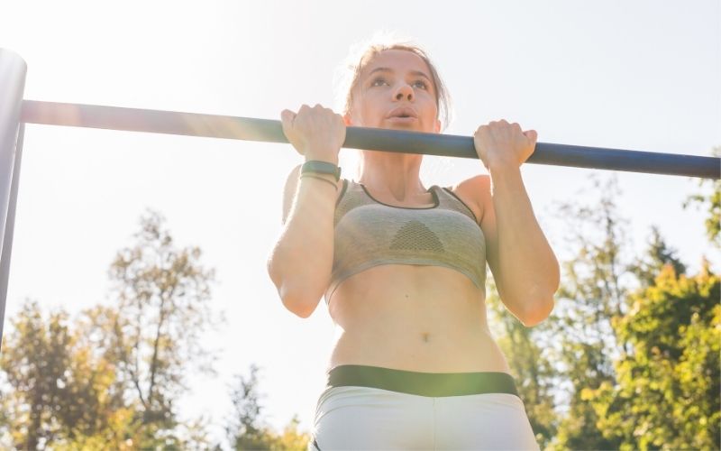 female doing chin ups outside