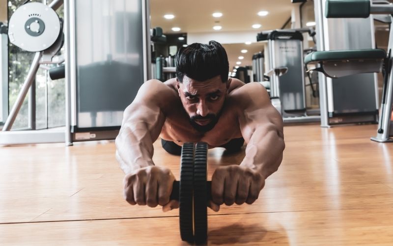 athletic man doing ab rollout in gym