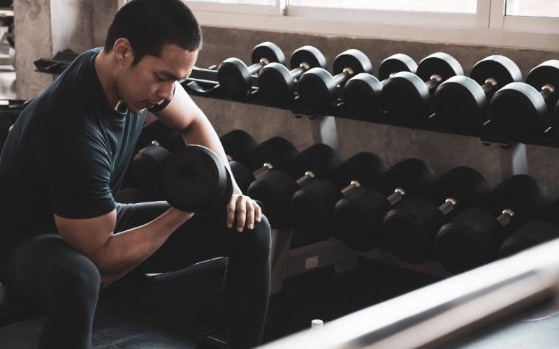 Asian man in black shirt and pants doing dumbbell curl.